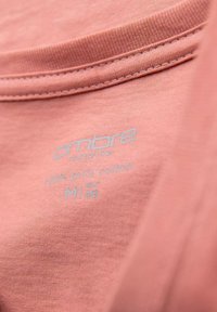 Etichetta di T-shirt in cotone di colore rosa chiaro, presenta "100% cotone puro", con testo stampato in blu; texture liscia e scollatura cucita.