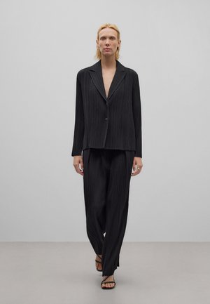 Costume noir à rayures, avec une veste ajustée et un pantalon à jambes larges, présentant un design épuré et un tissu léger.
