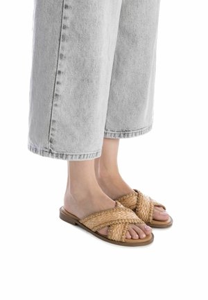 Chanclas trenzadas en tono marrón claro con un diseño de tiras cruzadas. Suela plana con una base marrón claro; adecuadas para un uso casual.