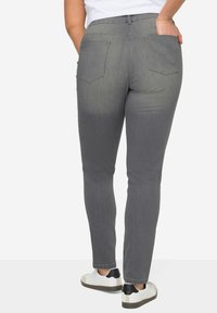 Jeans gris slim fit avec poches arrière et texture lisse, associés à des baskets blanches et noires. La taille est haute.