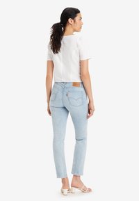 Valkoinen lyhythihainen crop-top, joka on yhdistetty vaaleansinisiin tiukkoihin farkkuihin, joissa on korkea vyötärö ja revitty helma, ja ne on yhdistetty valkoisiin korkokenkiin.