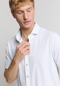 Witte short-sleeve shirt met een puntige kraag, gladde textuur en een knoopsluiting aan de voorkant. De hand van het model past de kraag aan. Nettere uitstraling.