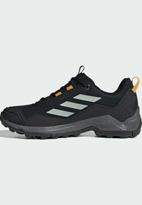 Zapatilla deportiva negra con un upper texturizado, acentos grises, logotipo reflectante de tres rayas, detalles de cordones en naranja y una suela resistente para tracción.