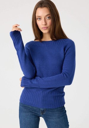 Suéter azul de punto con un escote amplio, puños y dobladillo acanalados, que presenta una textura suave y una silueta ajustada. Combinado con jeans de mezclilla.