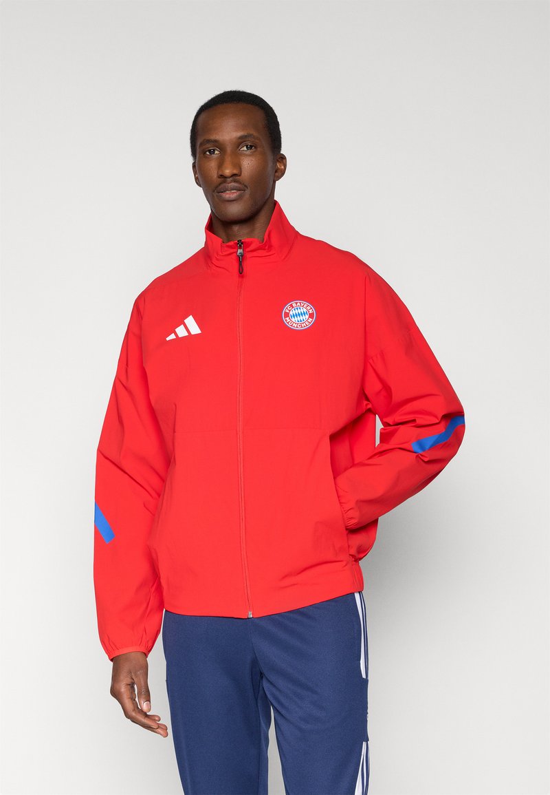 Red zip-up jacket made of lightweight material, featuring a high collar, blue accents on sleeves, and a logo on the chest.