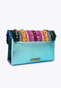 Borsa colorata in pelle turchese metallica, decorata con strisce di tessuto testurizzato, borchie e dettagli di perline. Plaque del marchio in tonalità oro esposta.