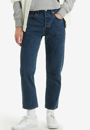 Dark blue denim jeans with a straight-leg fit, high waist, and five-pocket design. Worn with white sneakers and socks. Casual look.