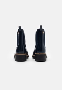 Stivaletti alla caviglia in vernice blu navy con pannelli elastici sui lati, linguetta per facilitare la calzata e suola in gomma nera con dettaglio beige cucito.