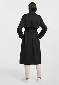 Czarny płaszcz trench z paskiem w talii, naramiennikami i długością do połowy łydki. Prosty design, gładka tekstura i zapięcie na guziki z tyłu.
