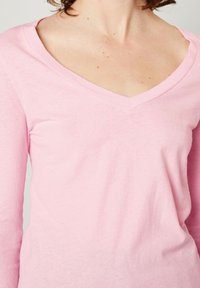 Maglietta rosa a maniche lunghe con scollatura a V realizzata in un tessuto morbido. Presenta una vestibilità rilassata e una texture liscia, adatta per l'abbigliamento casual.