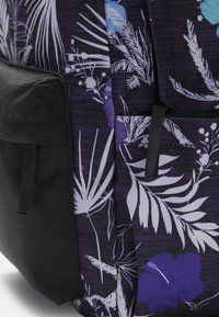 Mochila con una base negra y patrones florales en púrpura y azul. Incluye bolsillos con acentos de tela negra y superficie texturizada.