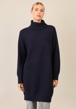 Abito turtleneck lavorato a maglia di colore blu navy, con vestibilità ampia, maniche lunghe e polsini e orli a coste. Texture liscia, arriva a metà coscia.