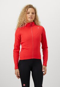 Rød zip-up jakke med høy krage og lange ermer, laget av elastisk materiale; har et lite logo på brystet og en tettsittende design.