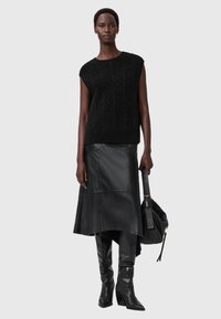 Top sin mangas de punto negro, falda midi de cuero y botas de tacón alto hasta la rodilla. Gran bolso negro con correa. Texturas suaves y diseño monocromático.