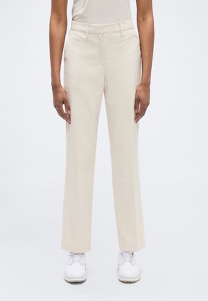 Bézs, testreszabott nadrág, lapos elejű, egyenes szárú szabással, két oldalzsebbel és finom textúrával. Fehér tornacipővel párosítva.