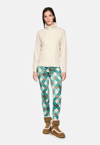 Light beige pullover with a high collar, patterned turquoise and brown leggings featuring a diamond design, and brown fur-lined boots.