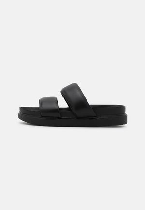 Sort slidesandal med to polstrede brede remme og en tyk flad sål, vist fra siden på en hvid baggrund.