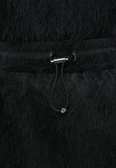 Vêtement noir en tissu texturé et duveteux. Comprend une fermeture à cordon avec une quincaillerie noire et un petit détail décoratif.