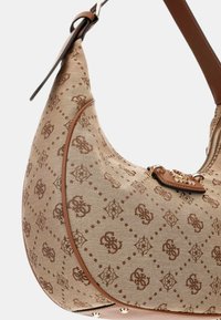 Un elegante bolso de hombro beige con una tela estampada y ribetes de cuero marrón, con una cremallera dorada y un detalle decorativo del logo.