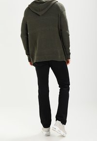 Mörkgrön luvtröja med ribbad textur, matchad med svarta byxor och ljusa sneakers. Fokuserar på en avslappnad, ledig passform.