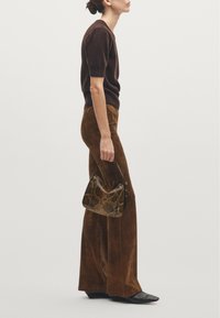 Brown knit sweater, brown suede flared pants, and black pointed-toe shoes. A brown snakeskin-patterned handbag completes the look.