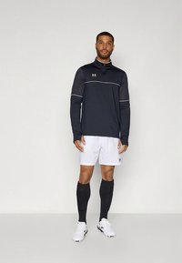 Juoda ilgarankovė sportinė palaidinė su baltais akcentais, derinama su baltais šortais ir juodomis kelių ilgio kojinėmis. Komplektą užbaigia balti sportiniai batai.