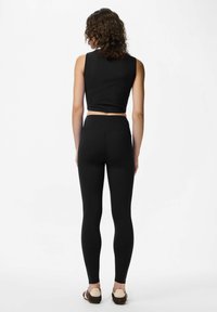 Top corto nero e leggings a vita alta, entrambi realizzati in tessuto elasticizzato, con un design elegante e una silhouette aderente.