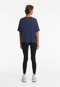 Sötétkék, oversized póló rövid ujjakkal, kerek nyakkivágással és egyenes szegéllyel, fekete leggings-szel és világos színű sportcipővel párosítva.