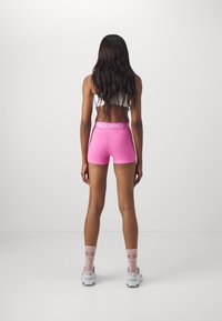Różowe sportowe szorty z białym pasem w talii, w połączeniu z białymi butami i różowymi skarpetkami. Szorty są dopasowane i mają gładką strukturę.