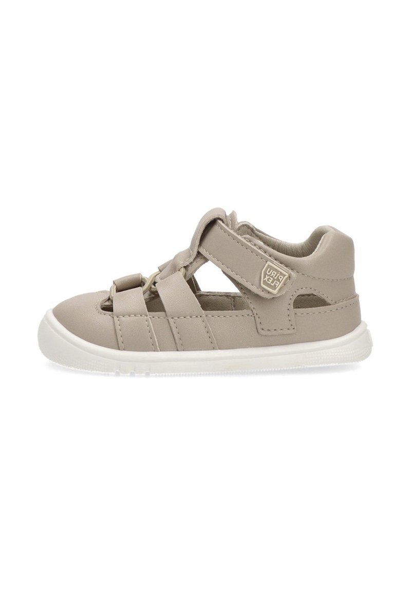 Zapatos infantiles de cuero beige con recortes, tira elástica y cierre de Velcro. Suela de goma blanca y detalle de marca discreto en el lateral.