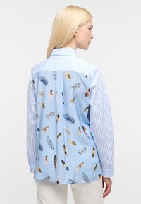 Light blue shirt with feather print, featuring a striped yoke and sleeves, buttoned cuffs, and relaxed fit with a curved hem.