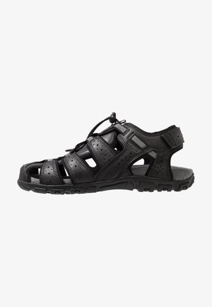 Black sport sandals featuring a closed toe, multiple straps, perforated design, rubber sole, and an adjustable toggle for a secure fit.