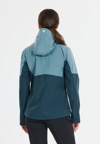 Water-resistant jacket in teal and dark navy. Features a hood, long sleeves, and a color-block design with a smooth texture.