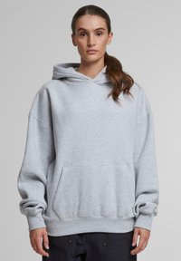 Svetlošedá mikina vyrobená z bavlnenej zmesi, s predným vreckom, širokými rukávmi a kapucňou so šnúrkou. Hladký povrch s rebrovanými manžetami.