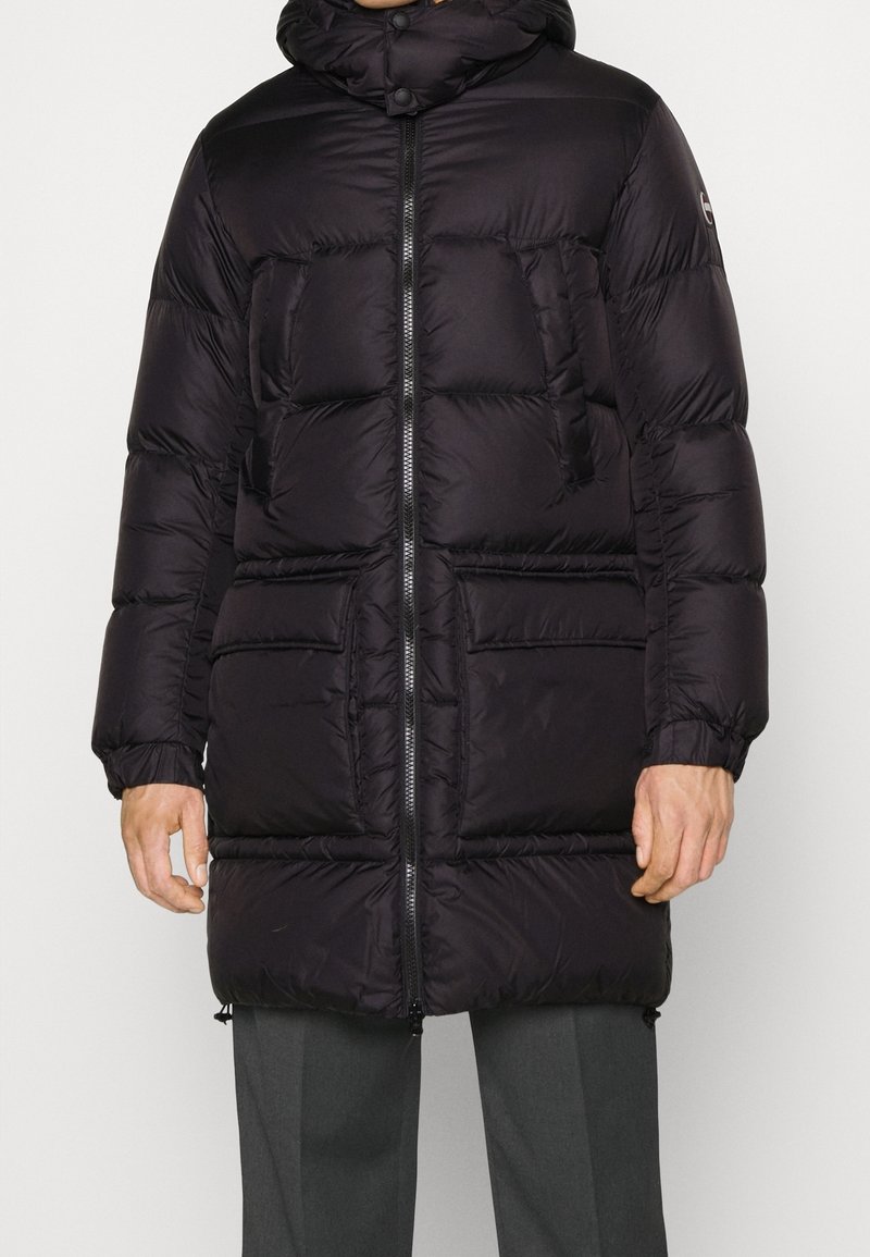 Svart pufferjacka med huva, dragkedja fram och flera framfickor; slät textur med kviltade sektioner för isolering.