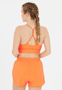 Klart orange atletisk crop-top med korsade remmar och matchande shorts. Slät textur med en figurnära design.