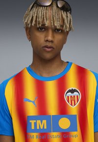 Camiseta del Valencia CF en rojo, amarillo y azul. Presenta un cuello redondo, un patrón degradado, el logo de Puma y un escudo del club en el pecho.