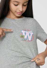 Szara koszulka z krótkim rękawem z graficznym wzorem przedstawiającym dużą literę "W" oraz kolorowy napis: "Keep Going" i "Let's Go" z przodu.