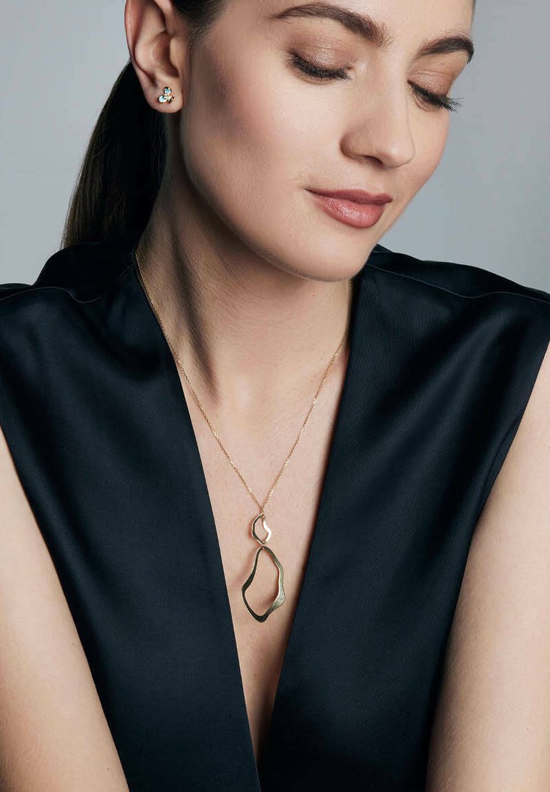 Kobieta z subtelnym uśmiechem, ubrana w czarną bluzkę z dekoltem w serek, prezentuje złotą biżuterię: naszyjnik z warstwowym wisiorkiem oraz pasujące kolczyki.