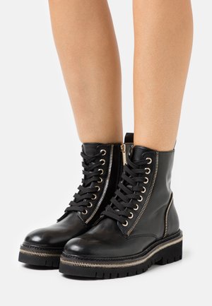 Black leather ankle boots with gold hardware, featuring front laces, side zippers, and a thick, textured rubber sole.