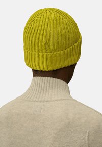 Cappello di maglia giallo brillante con texture a coste e risvolto, indossato sopra un maglione neutro a collo alto.