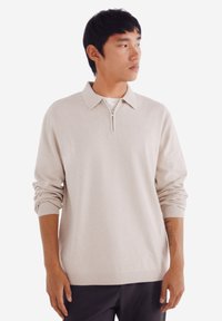 Beige gestrickter Polo-Pullover mit Reißverschlusskragen, langen Ärmeln und gerippten Bündchen. Glatte Textur, lässige Passform und minimalistisches Design.