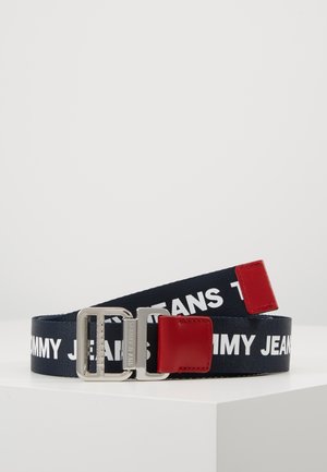 Ceinture en tissu noir avec texte blanc "Tommy Jeans", boucle métallique argentée et détails en cuir rouge aux deux extrémités.
