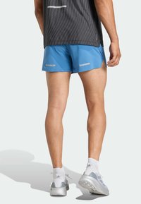 Pánske modré športové šortky s reflexnými prvkami, doplnené o sivé tenisky a biele ponožky, zobrazené zozadu. Športový strih.