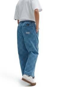 Modré deninové kalhoty s kostkovaným vzorem, elastickým pasem a viditelnými švy. Nošeny s bílými teniskami a obyčejným bílým tričkem.