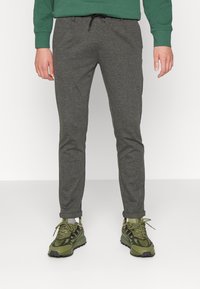 Pantalons de survêtement gris en mélange de coton, coupe slim avec taille à cordon, associés à des baskets vertes et noires avec des motifs de semelle distinctifs.