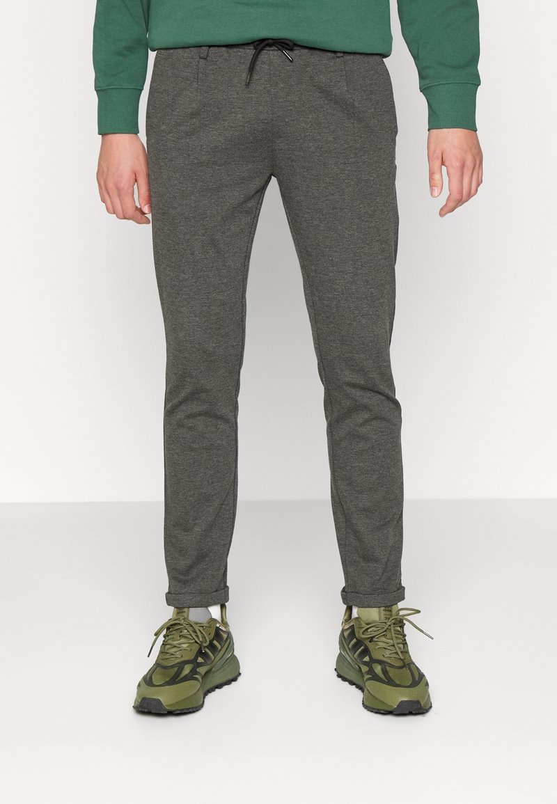 Pantalons de survêtement gris en mélange de coton, coupe slim avec taille à cordon, associés à des baskets vertes et noires avec des motifs de semelle distinctifs.