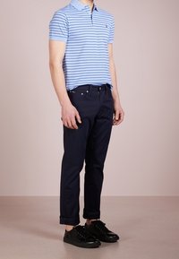 Světle modré pruhované polo tričko, námořnické chinos kalhoty a černé tenisky. Polo tričko má límeček a krátké rukávy. Chinos kalhoty jsou zúžené s vykulanými manžetami.