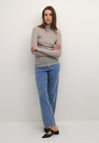 Maglietta grigia chiara a maniche lunghe con collo alto, abbinata a jeans blu a gamba larga e mule nere con tacco, che mostrano un look casual.