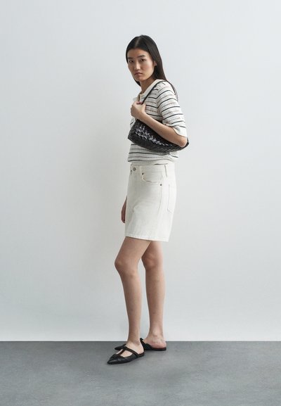 Saia de ganga branca, blusa de malha riscada em creme e preto, bolsa de mão tecida preta, sapatos planos pretos com bico fino. Fundo simples com chão cinza.